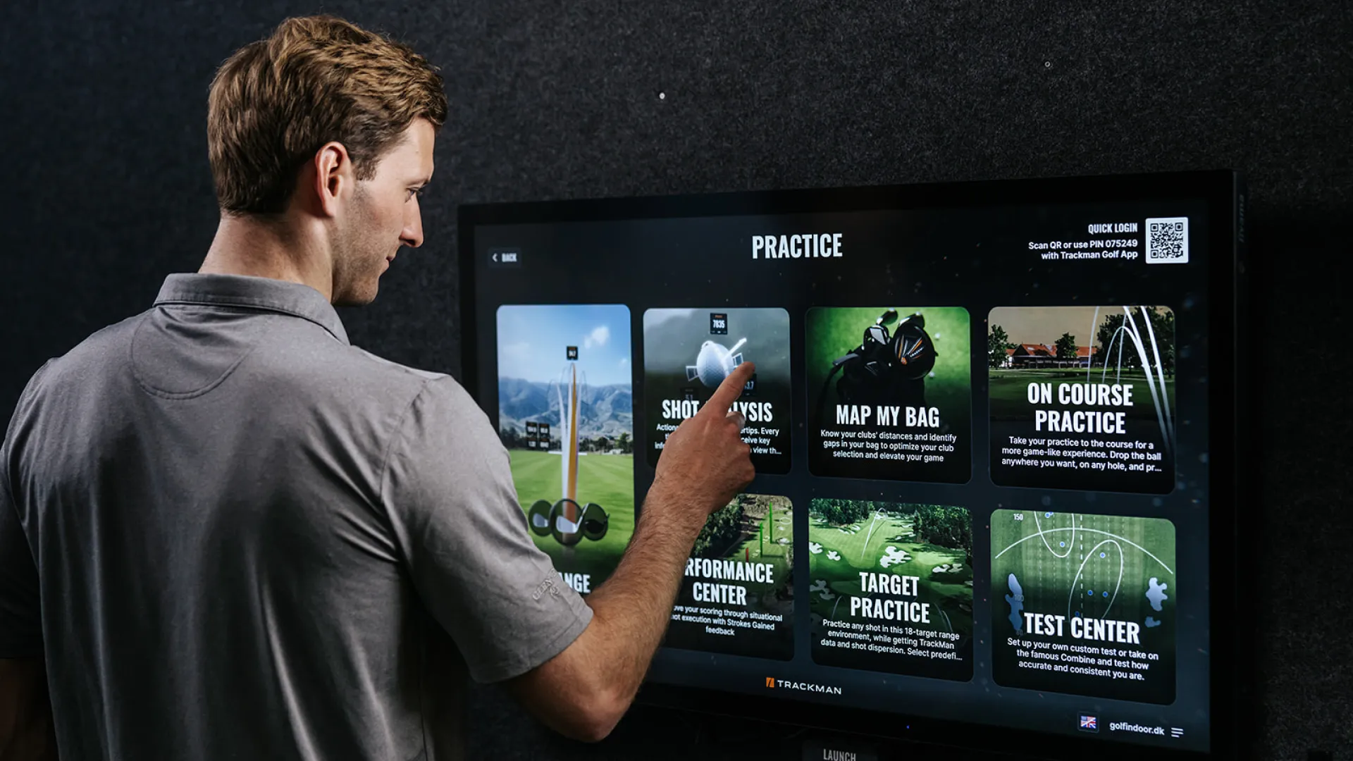 A person in a gray shirt interacts with a touchscreen displaying golf practice options, including shot analysis and target practice.