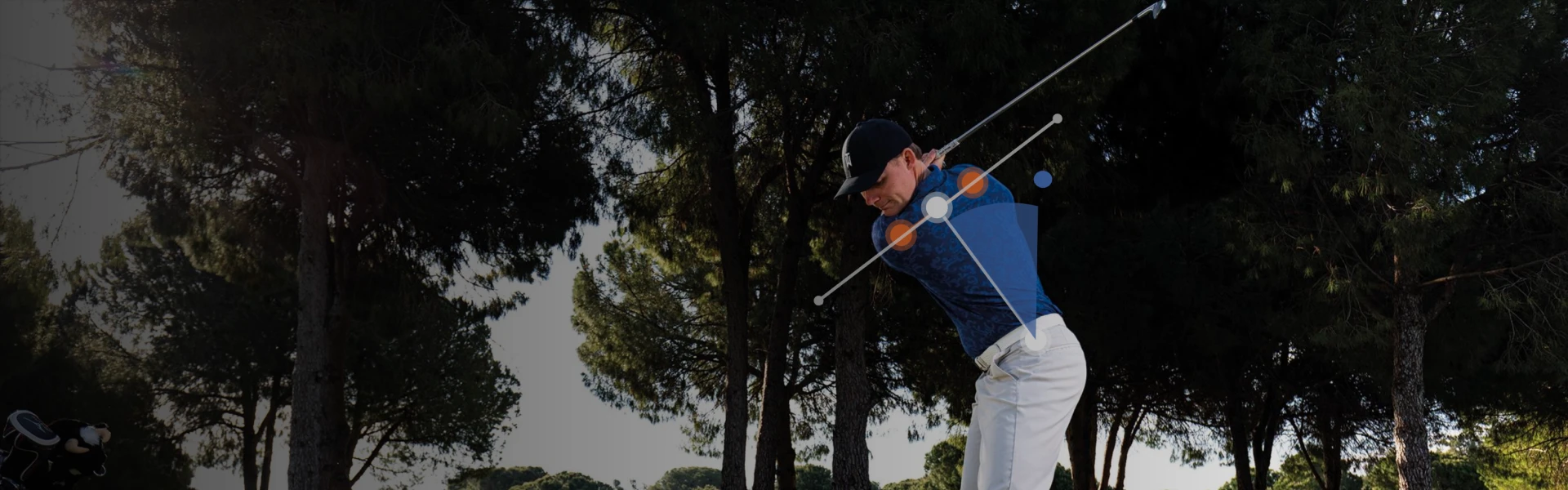 Golfer in blue shirt swings club, surrounded by trees. Blue and orange trajectory lines illustrate swing path and angles.