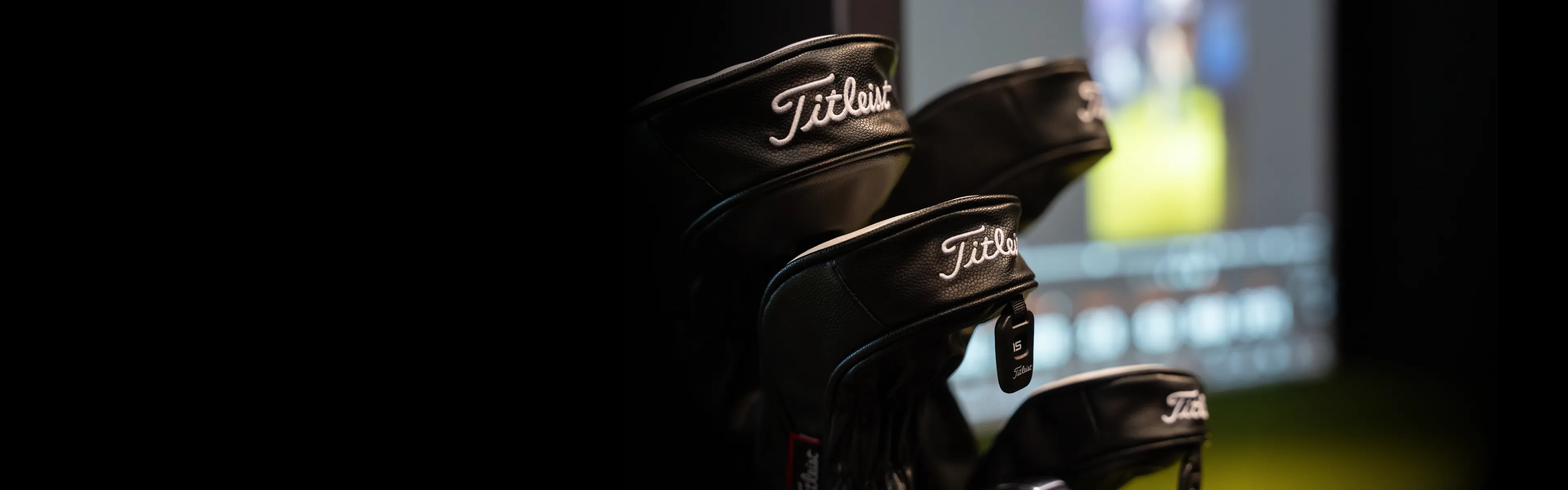 Close-up of golf club headcovers with the Titleist logo, set against a blurred indoor background.