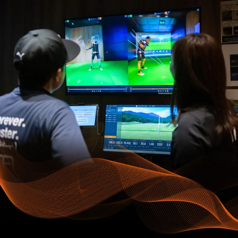 Two people viewing golf simulation screens with performance data. Wavy orange lines overlay in the foreground, adding a dynamic effect.