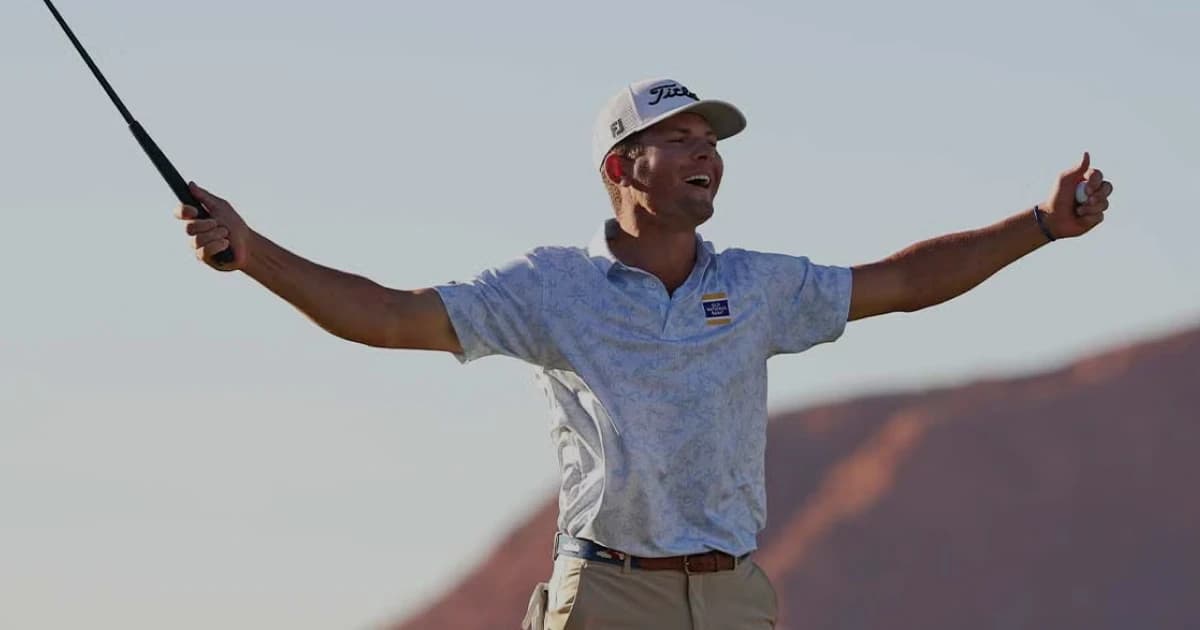 Golfer in a light blue shirt and cap celebrates with arms outstretched on a sunny day; mountains visible in the background.