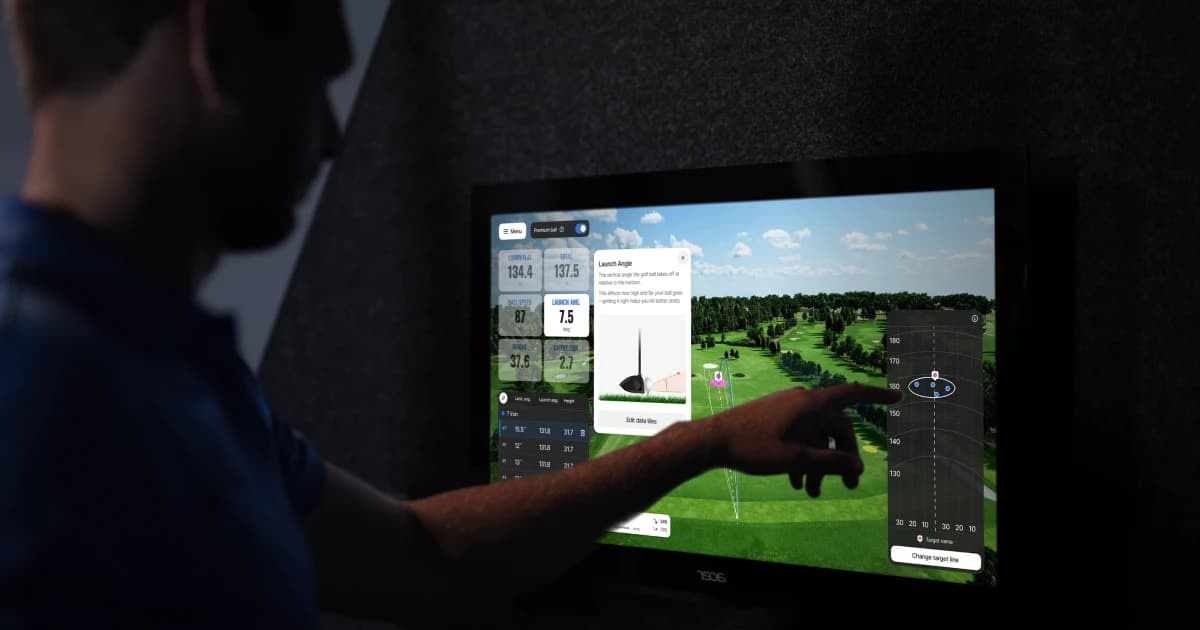 Person interacting with a golf simulator screen displaying data and a virtual golf course.