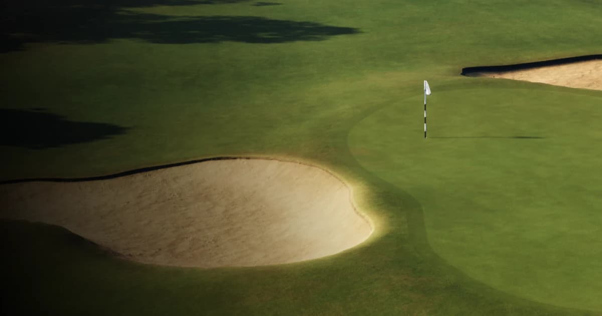 A golf course green with a flagstick, surrounded by sand bunkers, and shadows cast on the lush grass.