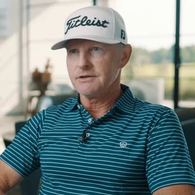 Man wearing a striped polo shirt and a Titleist cap, seated indoors with a blurred background.