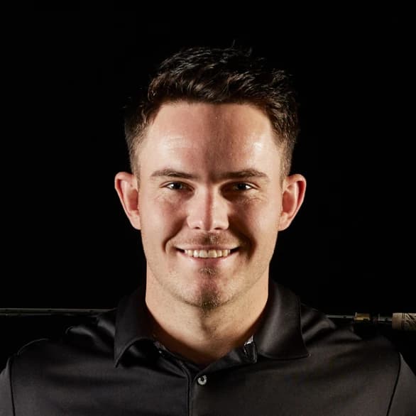 Smiling man with short dark hair, wearing a black collared shirt, against a dark background.