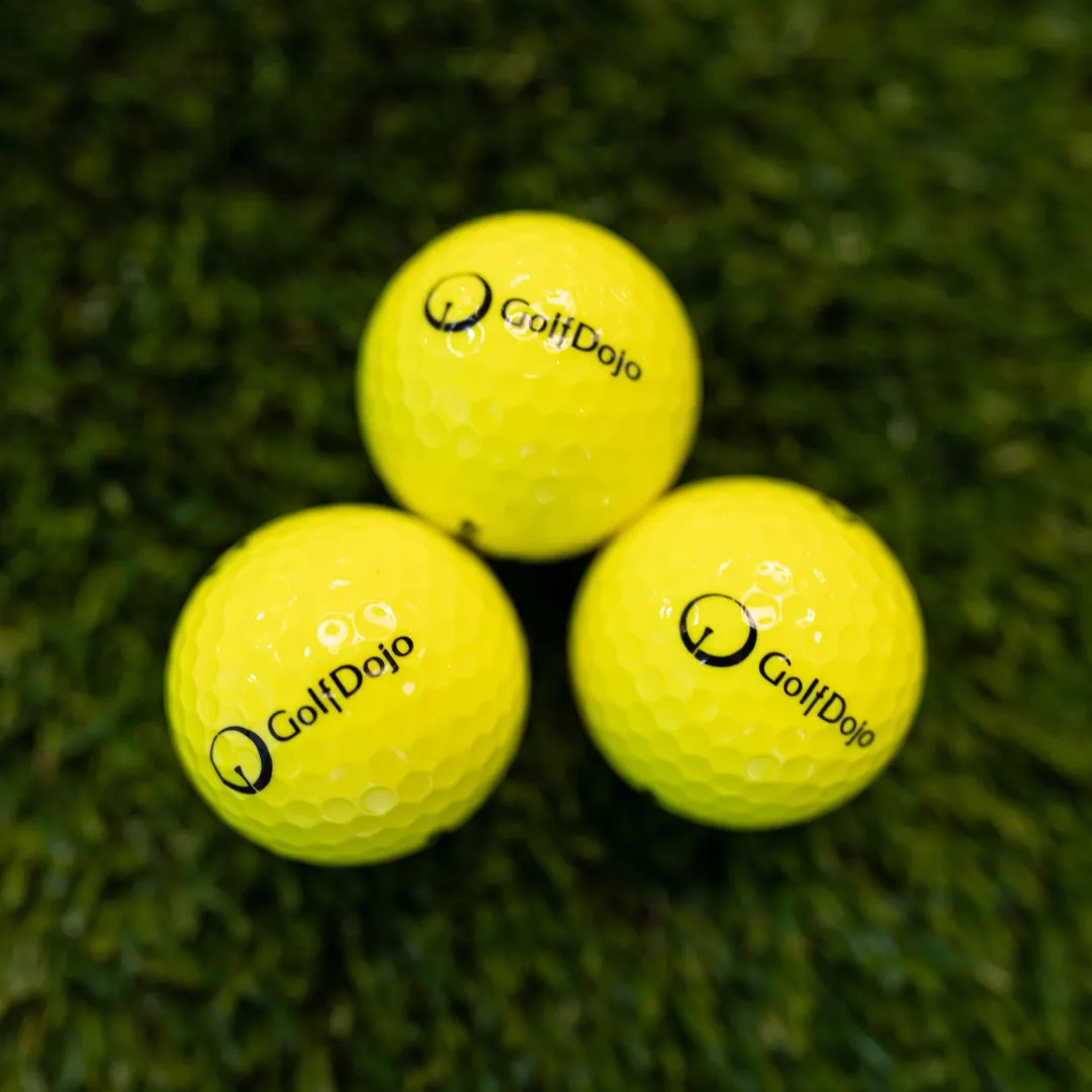Three yellow golf balls with "Golf Dojo" logo on grass.