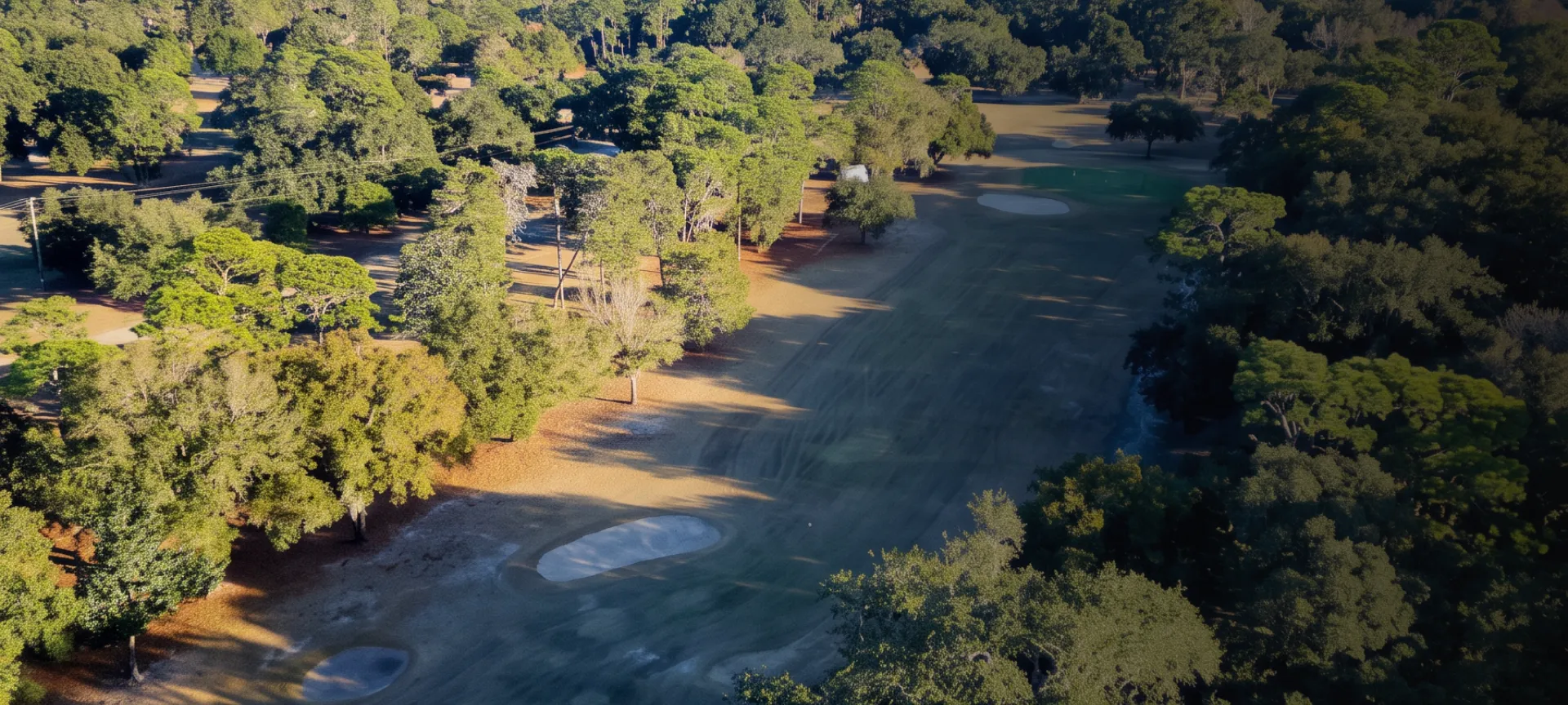 Aerial view of a golf course with lush green trees surrounding the fairway and sand bunkers under a clear blue sky.