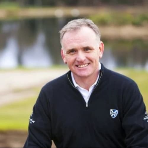 Smiling man in a dark jacket with a golf course background.
