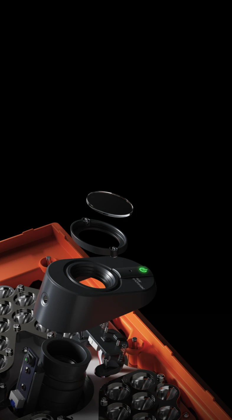 Close-up of a black camera lens assembly with an orange base, showing disassembled components against a black background.