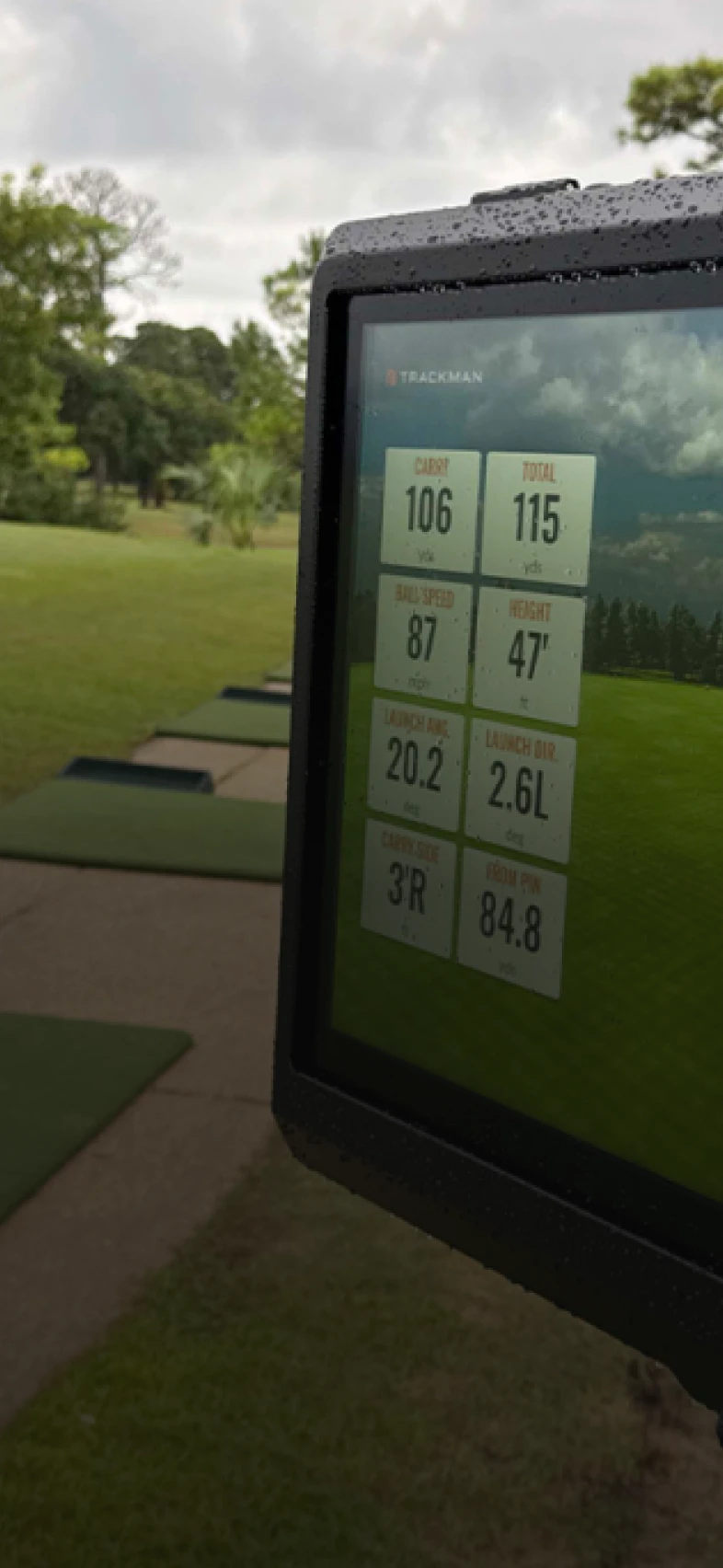 A digital screen displaying golf shot metrics like carry distance, total distance, ball speed, and launch angles against a grassy backdrop.