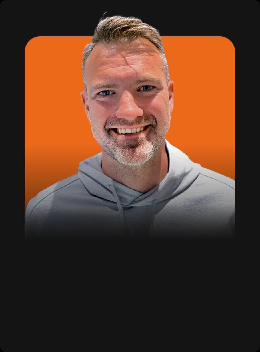 Smiling man in a gray hoodie against an orange background.